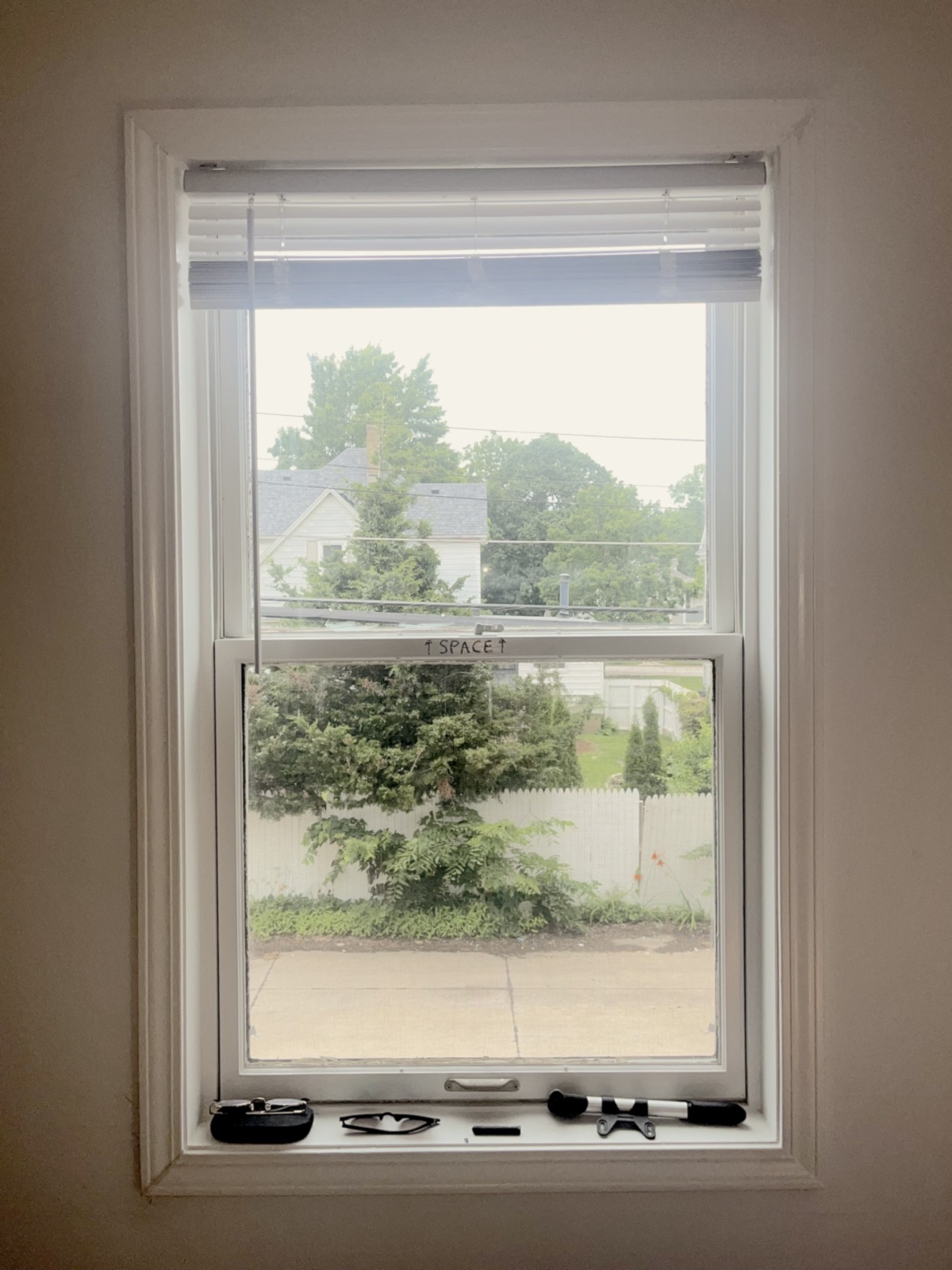 A window looking out onto a neighbourhood, with “↑ SPACE ↑” written in crayon across the glass